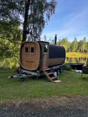 Set fra siden: TimberIN Nordic Square mobil sauna på trailer med skorsten ved en sø