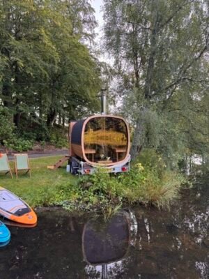 Bagende med panoramaglas på TimberIN Nordic Square mobil sauna på trailer ved en sø