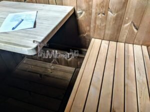 TimberIN Nordic Oval™ Terrace havesauna set tæt på indefra, med lys lægtebænk til højre, mørk gulvrist, sort ovnbeklædning til venstre og et infoark på hylden