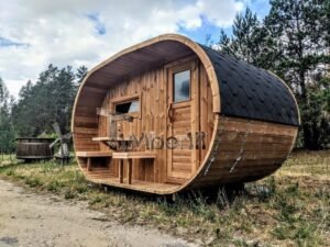 TimberIN Nordic Oval™ Terrace – udendørs sauna med terrasse, med synlig trædør, synligt vindue, sort tag og en bygning i baggrunden, i en anlagt have