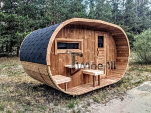 TimberIN Nordic Oval™ Terrace havesauna set fra venstre side i en lysning, med sort spåntag, bredt forrum, trædør, tværvindue og små siddebænke