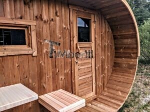 TimberIN Nordic Oval™ Terrace – udendørs sauna med terrasse, med indstigningstrappe i træ, synlige træbænke, synlig trædør og synligt vindue, i en anlagt have
