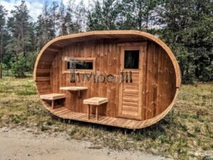 TimberIN Nordic Oval™ Terrace – udendørs sauna med terrasse set indefra, med synlige træbænke og en bygning i baggrunden, i en anlagt have