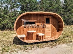 TimberIN Nordic Oval™ Terrace – udendørs sauna med terrasse, med synlige træbænke, synlig trædør og gamle træer i baggrunden, på en åben eng