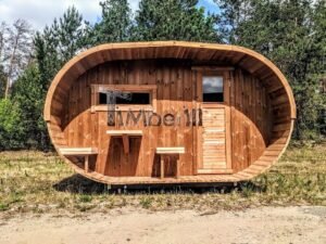 TimberIN Nordic Oval™ Terrace havesauna set lige forfra på en solrig eng, med dybt ovalt forrum, tværgående vindue til venstre, dør til højre og udendørs bænke
