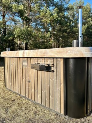 TimberIN Nordic Square™ Acryl vildmarksbad set fra siden ved skovkanten, med lys lodret træfacade, hvid kant og sort teknik- eller ovnmodul til højre