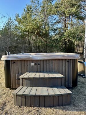 TimberIN Nordic Square™ Acryl – kvadratisk vildmarksbad i akryl, med indstigningstrappe i træ og gamle træer i baggrunden, i en anlagt have