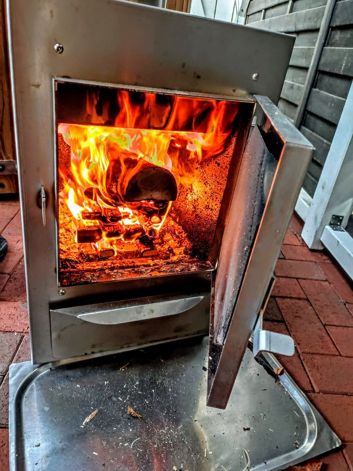 Brændeovn med åben låge og kraftige flammer fra tørt brænde ved et vildmarksbad