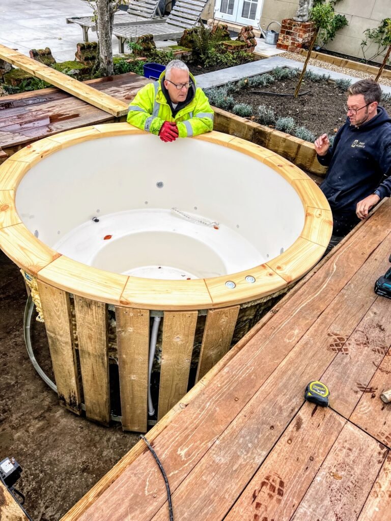 Indbyg vildmarksbadet i en terrasse: forberedelse og installation 2 To montører placerer et vildmarksbad med hvid indsats i en åbning i terrassen