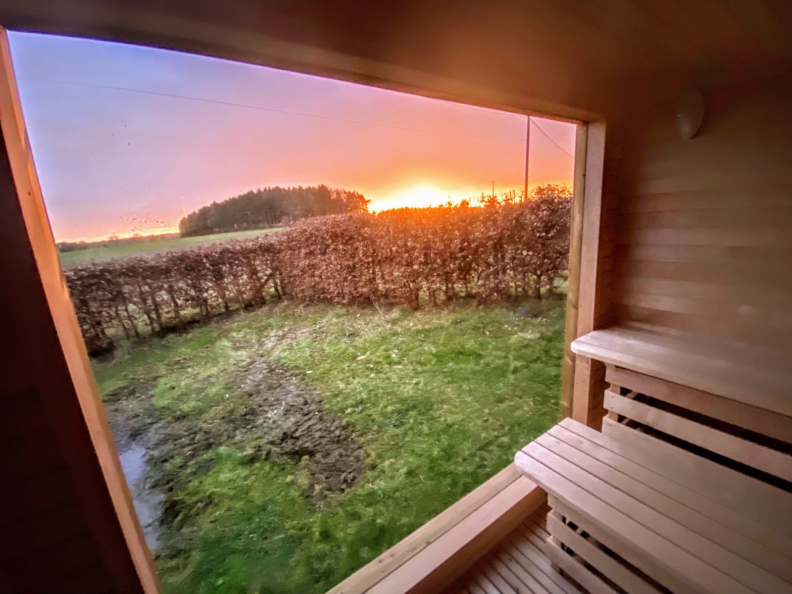 Hvor varm skal en sauna være? 1 Udsigt gennem saunavinduet ved solnedgang med træbænke i forgrunden