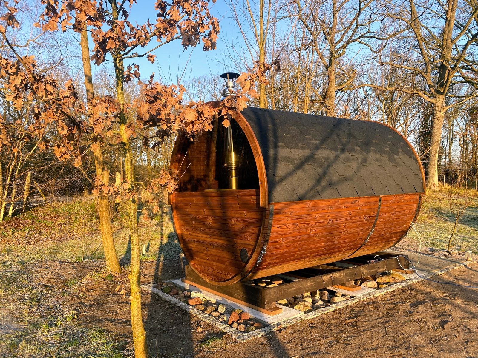 Saunatønde – tønde sauna til haven 1 Saunatønde i træ med panoramaende og mørkt tag i en have med efterårstræer