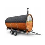 TimberIN Nordic Nomad™ – mobil tøndesauna med korpus i termotræ, panoramafront i glas, skorsten til brændeovn og toakslet vejtrailer på hvid baggrund.