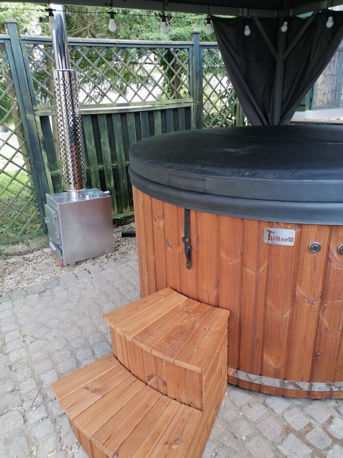 Vildmarksbad med låg og ekstern brændeovn i rustfrit stål under en pavillon med gardiner