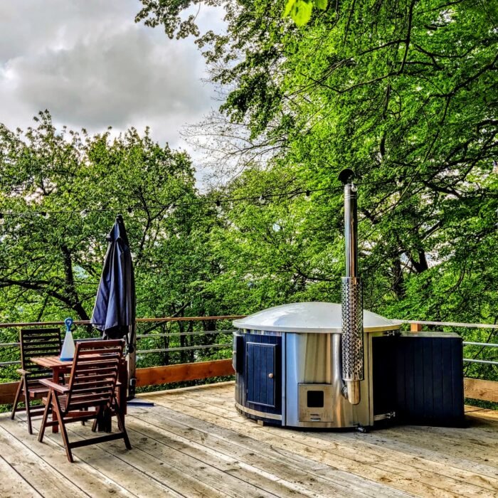 Vildmarksbad med udvendig brændeovn og skorsten på en terrasse ved skoven